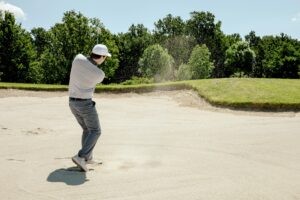 Golfer executing a sand bunker shot on a sunny day